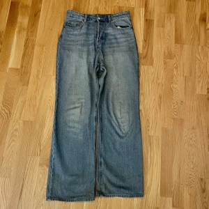 Blå jeans från H&M - Säljer ett par  blå jeans från H&M i storlek 38. De har en klassisk knappgylf och är i en loose fit med hög midja. Perfekta för en avslappnad stil och passar till alla säsonger. Lite slitna detaljer för en cool look! ( sliten mellan benen)