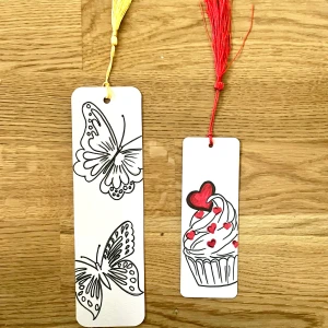 Handgjorda bokmärken - Två handgjorda bokmärken, ett med svartvita fjärilar och gult snöre, och ett med en färgglad cupcake med hjärtan och rött snöre. Perfekta för att hålla koll på läsningen med stil!