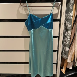 Turkos och blå sidenklänning - Säljer en elegant turkos och blå klänning i siden med smala axelband. Perfekt för sommarens fester eller en speciell kväll. Klänningen har en vacker glans och en figurnära passform som ger en lyxig känsla. Hör av dig vid intresse!