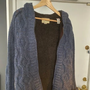 Kabel stickad hoodie - Super skön och mysig hoodie från märket energie, perfekt nu till hösten och vinter. Den är väldigt varm och snygg men ändå dåliga är en liten vit färg stänk (se sista bilden) annars är den i jätte bra skick!