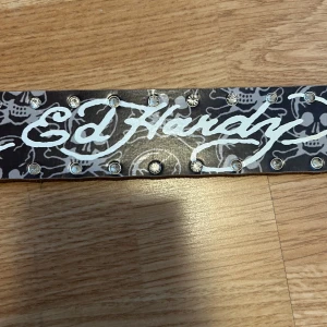 Bälte - Ed Hardy bälte. Strass som går längs båda kanterna. Några stenar/strass har ramlat av men inget som märks super tydligt enligt mig. Mått: Hela bältet är 126 cm långt. Första hålet är efter 83 cm. Bältet är ca 4 cm brett. Skicka gärna prisförslag om du kan tänka dig något annat! 