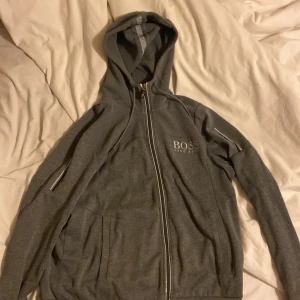 Grå og Hugo boss hoodie - Hugo boss hoodie. Inga fläckar eller hål men kedjan är lite förstörd men inte direkt sönder. Säljer den för att jag inte använder längre. Original pris ligger runt 1300kr. Storlek L men passar M perfekt oxå.