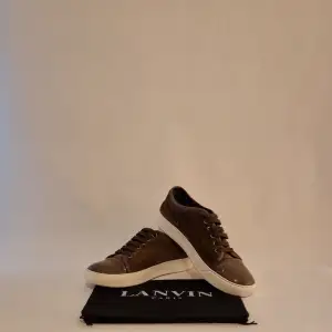 Säljer ett par snygga bruna sneakers från Lanvin i bra skick. De har en stilren design med snörning och en vit sula som ger en fräsch kontrast. Perfekta för både vardag och fest! Kommer med originalpåse!