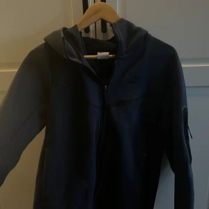 Mörkblå tech fleese - Säljer min Nike tech fleece i mörkblå då jag inte använder den längre. Några slitningar i vänstra armen uppe vid axeln men inget som syns. Skick 8/10