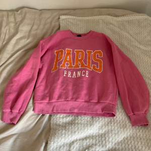 Säljer en superfin rosa sweatshirt från Gina Tricot med texten 'PARIS FRANCE' i stora bokstäver på framsidan. Den är gjord av bomull/polyester, är perfekt för en avslappnad stil. Lite oversize passform och är riktigt skön att ha på sig💕