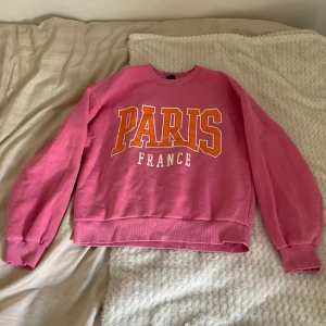 Rosa sweatshirt från Gina Tricot - Säljer en superfin rosa sweatshirt från Gina Tricot med texten 'PARIS FRANCE' i stora bokstäver på framsidan. Den är gjord av bomull/polyester, är perfekt för en avslappnad stil. Lite oversize passform och är riktigt skön att ha på sig💕