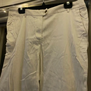 Vita byxor från H&M - Säljer ett par vita byxor från H&M i storlek EUR 44. De har en klassisk design med knapp och dragkedja framtill. Perfekta för en stilren look!