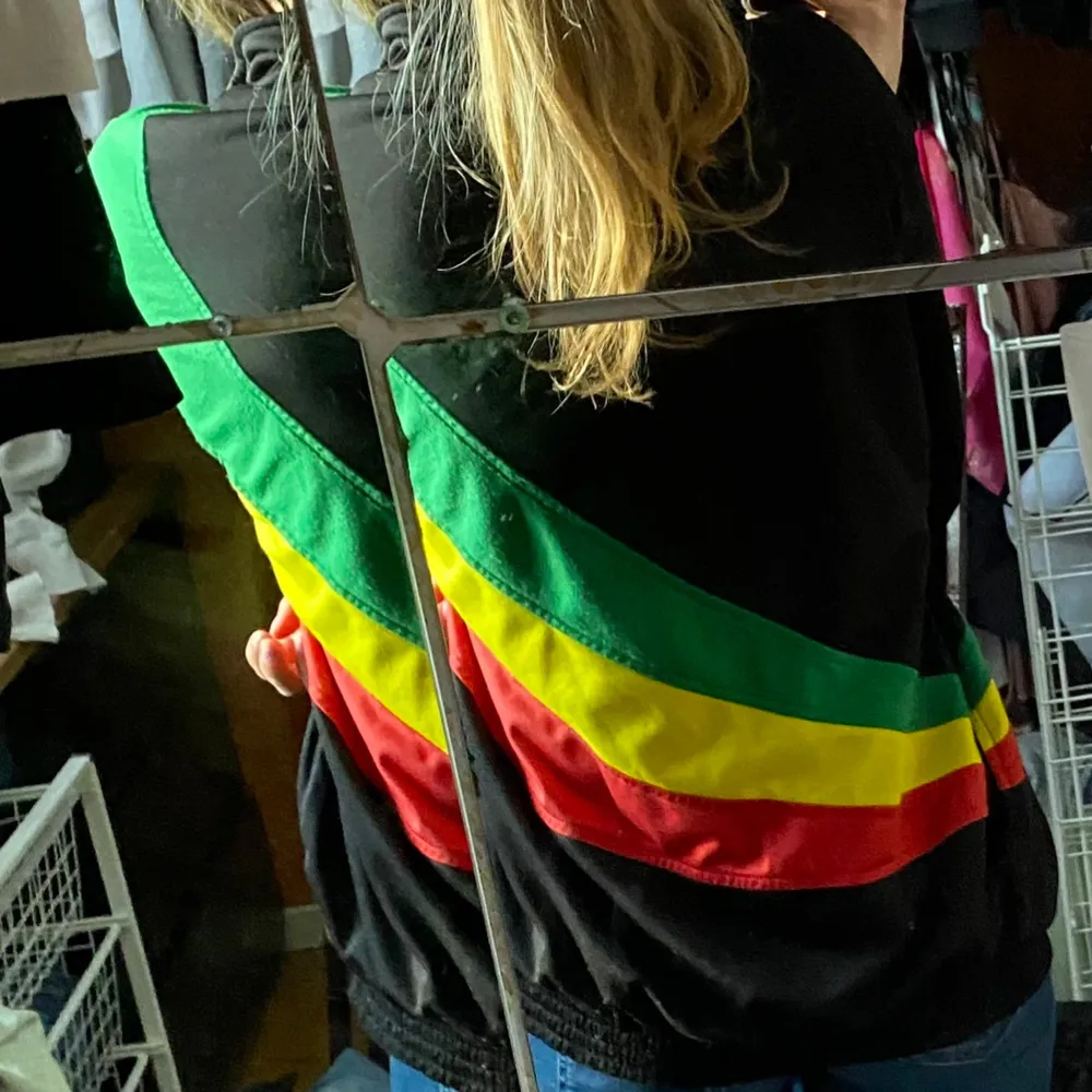 Säljer en svart jacka med Bob Marley-tryck och färgglada detaljer i rött, gult och grönt. Jackan har en dragkedja framtill och långa ärmar. Perfekt för dig som gillar reggae och vill ha en färgglad stil!. Jackor.