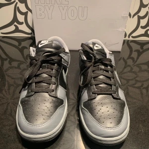 Nike Dunk i svart och grått - Säljer ett par Nike Dunk sneakers i en snygg kombination av svart och grått. Skorna är användna få antal gånger. Det är Nike dunk Low by you. Det står STEN på baksidan av skon.