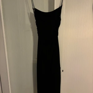 Svart lång klänning - Säljer en svart lång fin klänning från Zara i storlek M har en öppen rygg med snöre Helt nytt prislappen sitter kvar 