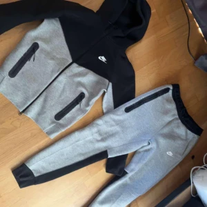 Grå och svart hoodie från Nike - Säljer en snygg och bekväm grå och svart hoodie från Nike. Den har en dragkedja framtill och praktiska fickor med dragkedjor. Perfekt för träning eller en avslappnad dag. Hoodien har långa ärmar och en skön huva.