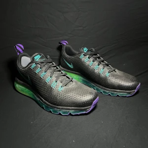 Nike Air Max med grön och lila sula - Size 10.5 US/EU 44.5 Nike Air Max Motion ’631767-001’ Säljer ett par snygga Nike Air Max sneakers i svart med en cool grön och lila sula. Skorna har en perforerad design för bra ventilation och en bekväm passform.