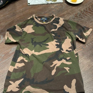 Camouflage t-shirt från Polo Ralph Lauren - Säljer en cool camouflage t-shirt från Polo Ralph Lauren. Den har en klassisk rund hals och en bröstficka. Perfekt för en avslappnad stil. 14-16 år i barnstorlek men Ralph lauren har stora storlekar jag är 168cm och den är lite liten på mig. Skriv gärna om ni har funderingar🙌