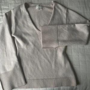 Beige v-ringad stickad  tröja från H&M - Säljer en stilren beige tröja från H&M med v-ringning och långa utgående  ärmar. Tröjan har ribbade detaljer vid ärmslut och nederkant, vilket ger en snygg touch. Perfekt för en avslappnad och chic look.