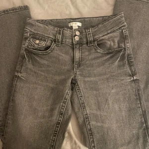 Grå jeans från Gina Tricot Young - Snygga grå jeans från Gina Tricot med två knappar i midjan och klassiska femficksdesign. De har en liten bootcut passform och är perfekta för en avslappnad stil. Säljer för att de är för korta för mig🎀