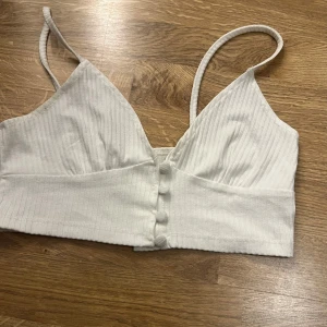 Vit ribbad linnetopp från Glamorous - Säljer en stilren vit ribbad linnetopp från Glamorous. Toppen har smala axelband och knappar framtill. Perfekt för varma dagar eller som ett lager under en kavaj.