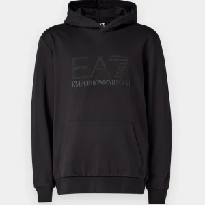 Svart hoodie från Emporio Armani - Snygg svart hoodie från Emporio Armani med EA7-logga på bröstet. Den har en klassisk design med huva och en stor ficka framtill. Perfekt för en stilren och bekväm look. Endast testad men de blev fel storlek Ny pris 1645 