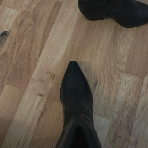 Svarta cowboy boots med spetsig tå - Snygga svarta cowboy boots i skinn med spetsig tå och dekorativa sömmar. De har en dragkedja på sidan för enkel på- och avtagning. Perfekta för en stilren look med en touch av western. Aldrig använda! 