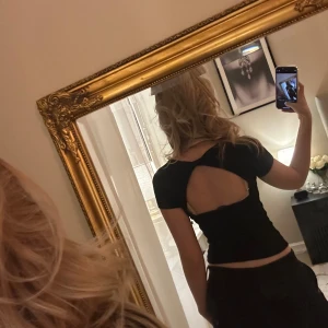 Svart topp med öppen rygg - Snygg svart topp med en stilren design och öppen rygg. Toppen har korta ärmar och en dragkedja framtill för en modern look. Perfekt för en kväll ute eller en speciell tillställning. Fyrkantig urringning 