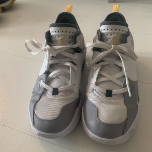 Nike Air Jordans i vitt och grått - Snygga Nike Air Jordans i vitt och grått med gula detaljer. Skorna har en modern design med snörning och perforerade sidor för extra ventilation. Perfekta för både stil och komfort. De har fortfarande brs traktion och sitter jätte brs runt fötterna 