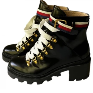 Svarta Gucci  boots med snörning  - Snygga svarta boots i skinn med vita snören och dekorativa ränder i rött och blått runt ankeln. Skorna har en robust sula och guldfärgade detaljer som ger en lyxig känsla. Perfekta för att ge din outfit en stilfull touch. Kartong, taggar och dustbag medföljer.