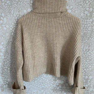 Beige ribbad polotröja - Säljer en snygg beige ribbad polotröja med långa ärmar. Tröjan är croppad och har en hög polokrage som ger en stilren look. Perfekt för kyligare dagar!