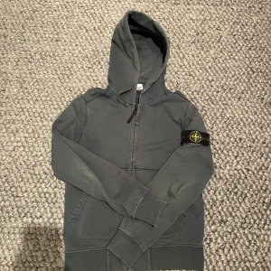 Stone Island Zip Hoodie - Tja, säljer en mörkgrön zip Hoodie för Stone Island. Hoodie är riktigt nice och snygg och passar dig bäst som är mellan 165-170. Självklart äkta✅. Bevis kan skickas vid önskning. Alla tags och label finns kvar på Hoodien (kolla bilderna).OBS bilden visar lite gråare färg, den är mörkgrön! 👌