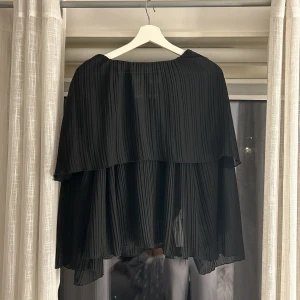 Svart blus från Zara - Snygg svart blus från Zara med plisserad design och löst fall. Blusen har en knytning i ryggen och är perfekt för en elegant look. Den är tillverkad i ett lätt och luftigt material som ger en skön känsla. Kontakta mig för fler frågor💕