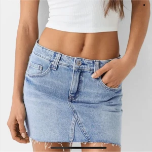 Blå jeanskjol - Säljer en snygg blå jeanskjol med fransig nederkant och klassisk femficksdesign. Kjolen har en kort längd och en rå kant som ger en trendig look. Perfekt för en avslappnad stil. St 32