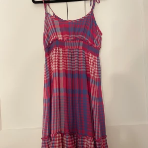 Rutig klänning från Peak Performance - Snygg rutig klänning i rosa och blått från Peak Performance. Klänningen har en smockdetalj i midjan och är ärmlös, vilket ger en luftig och bekväm känsla. Perfekt för varma dagar med sin lätta och flödande design. Helt oanvänd. Köpare står för frakten!🩷