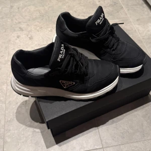 Svarta sneakers från Prada - Snygga svarta sneakers från Prada med vit sula och klassisk snörning. Perfekta för en stilren look. Diskret Prada-logga på sidan och tungan.