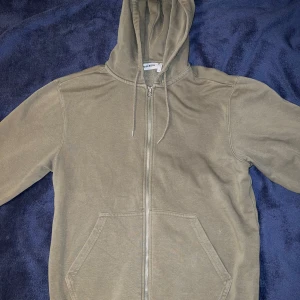 Grön hoodie från Weekday - Säljer en stilren beige hoodie från Weekday i storlek XS. Den har en dragkedja framtill och en praktisk huva med snörning. Perfekt för en avslappnad look. Funkar för både tjejer och killar! 