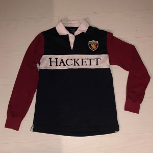 Pikétröja från Hackett - Marinblå pikétröja från Hackett med vinröda ärmar och vit krage. Tröjan har en broderad logotyp på bröstet och knappar vid halsen. Vid frågor eller fler bilder kontakta mig. Priset går att diskutera. 