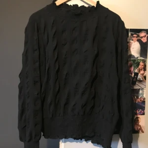 Svart långärmad blus - Snygg svart blus med lång ärm och unikt texturerat mönster. Blusen har en knapp i nacken . Blusen tror jag är ifrån Vila lappen är avklippt 