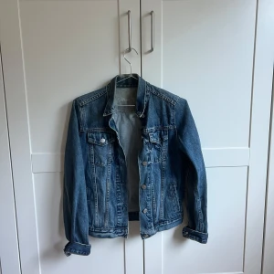 Blå jeansjacka från Gap - Säljer en klassisk blå jeansjacka från Gap i storlek XS. Jackan har en normal passform med knappar framtill och två bröstfickor. Perfekt till våren och sommaren! Säljer för 200kr + frakt