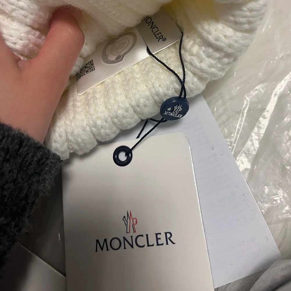 Två stilrena stickade mössor från Moncler i svart och vit. Båda mössorna har en stor tofs på toppen och Monclers logotyp framtill. Perfekta för att hålla värmen under kalla dagar.. Asusteet.