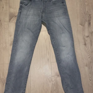 Grå jeans från Jack & Jones - Snygga grå jeans från Jack & Jones i modellen Slim/Glenn. De har en slim passform och är perfekta för en stilren look. Klassisk design med knappar och dragkedja framtill. Storlek W33 L34.För bättre bilder skriv gärna! Det blev nått fel när jag skulle ladda upp bilderna så det är därför man inte ser hela bilden.
