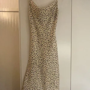 Vit ”prickig” klänning från Gina Tricot - Säljer en stilren vit klänning med svarta prickar och smala axelband. Klänningen har en v-ringad design och är perfekt för sommarens varma dagar. Den är figurnära och ger en elegant look. Inköpt på Gina Tricot och knappt använd. Säljer pga att den aldrig kommer till användning 🩷