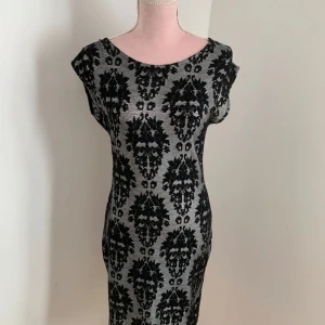 Grå och svart mönstrad klänning - Snygg grå klänning med svart mönster. Den har en tight passform och korta ärmar, perfekt för en stilren look. Klänningen är gjord i ett mjukt material som känns skönt mot huden.