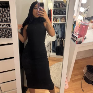 Svart ärmlös klänning - Snygg svart ärmlös klänning med hög hals och figurnära passform. Perfekt för en stilren look.