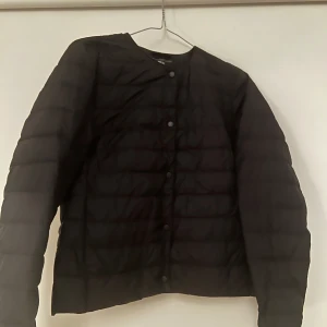Svart pufferjacka - Säljer en svart dunjacka i bra skick. Den har en stilren design med knappar framtill och långa ärmar. Perfekt för höst och vår. Jackan är lätt och bekväm att bära. Passar bra att ha som extra lager under en tjockare jacka 