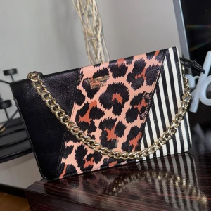 Leopardmönstrad väska från Victoria's Secret - Snygg kuvertväska med leopardmönster och randiga detaljer från Victoria's Secret. Väskan har en guldfärgad kedja och är perfekt för en utekväll. Insidan är randig och har plats för det viktigaste. En riktig statement piece för den modemedvetna!
