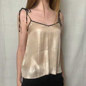 Glansigt  linne med svarta band - Beige/rosa linne med glansigt material och svarta band som knyts vid axlarna. Perfekt för en utekväll eller fest!