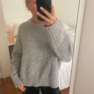 Grå stickad tröja - Mysig grå stickad tröja perfekt för kyliga dagar. Den har en avslappnad passform med långa ärmar och ribbade muddar. Perfekt för både höst och vinter. Superbekväm och lätt att matcha med olika outfits!