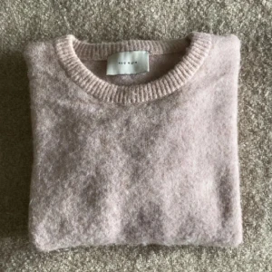 Ljusrosa ulltröja från Neo Noir - Mysig ljusrosa tröja från Neo Noir i ullblandning. Perfekt för kyliga dagar med sin mjuka och varma känsla. Tröjan har en klassisk rund hals och långa ärmar, perfekt för vardag och hemmamys! Den är sparsamt använt och försiktigt omhändertagen. 