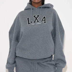 Grå hoodie från LXA The Label - Säljer en snygg grå hoodie från LXA The Label. Den har en stor logga på bröstet och en bekväm passform med långa ärmar och justerbar huva. Perfekt för en avslappnad stil eller mysiga dagar hemma. 🩶