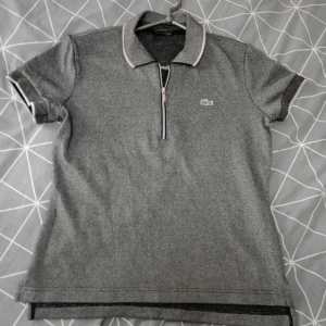 Lacoste piké - (Nyskick) Säljer en stilren slivrig pikétröja från Lacoste i mycket bra skick. Tröjan har en klassisk krage med dragkedja och korta ärmar. Perfekt för en avslappnad men ändå snygg look. 🐊