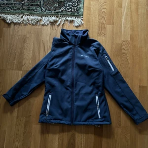 Mörkblå jacka från Columbia - Säljer en mörkblå jacka från Columbia i mycket bra skick. Den har en dragkedja framtill och praktiska fickor med dragkedjor, inklusive en på ärmen. Jackan är perfekt för höst och vår, med ett mjukt fleecefoder för extra värme. Passar bra för utomhusaktiviteter och vardagsbruk.