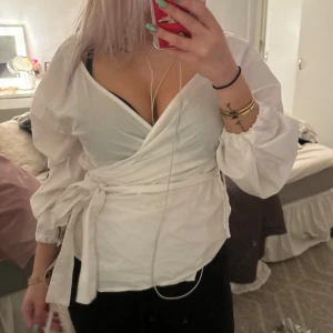Vit omlottblus - Säljer en superfin vit omlottblus med knytband i midjan. Blusen har långa puffiga ärmar och en djup v-ringning som ger en elegant look. Perfekt för både vardag och fest! 🕊️