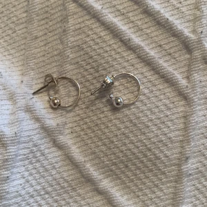 Små silverörhängen med kulor - Säljer ett par stilrena små silverörhängen i form av ringar med en liten kula på varje. Perfekta för både vardag och fest! De är i mycket bra skick och ger en minimalistisk touch till vilken outfit som helst. Passar bra till alla säsonger och är lätta att matcha med andra smycken.